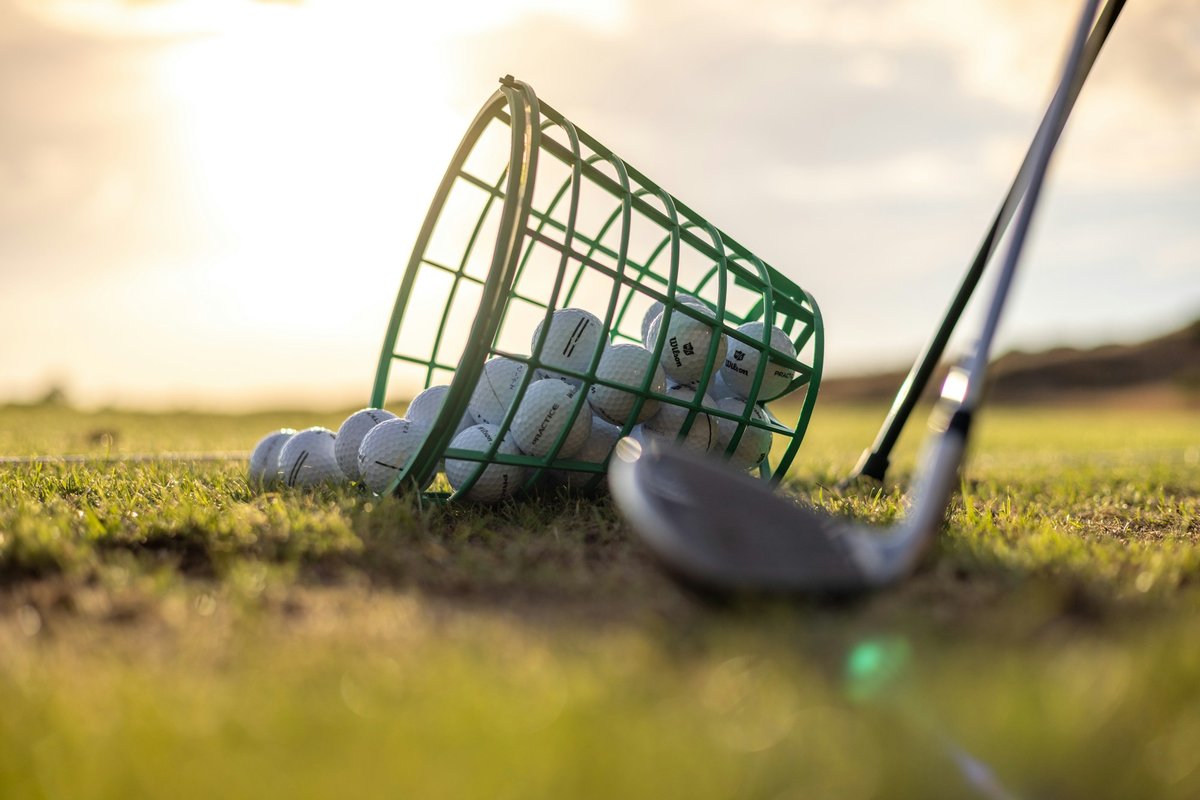 Panier de balles de practice renversé sur l'herbe à côté d'un fer de golf, lumière du soir